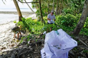 The Mieco Beach Yacht Club's Lanny Pirtle tosses a bottle into a waste collection bag at Enemanet Island. Photo: Mika Makelainen.